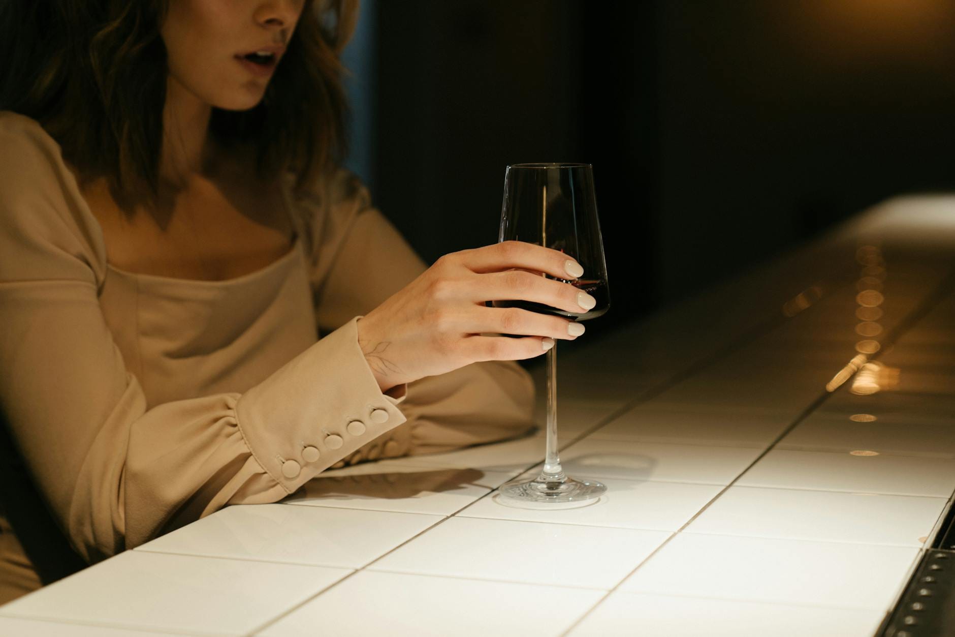 Kobieta w eleganckiej sukience samotnie siedzi przy barze z kieliszkiem wina