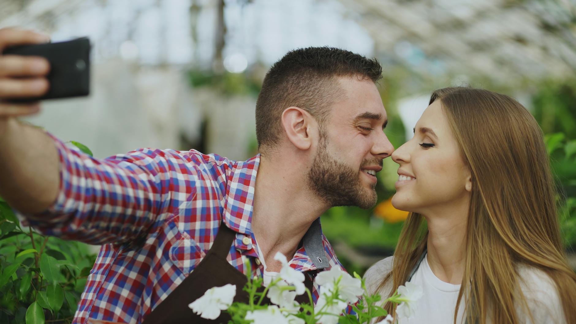 Uśmiechnięta para robi selfie w otoczeniu zieleni w szklarni